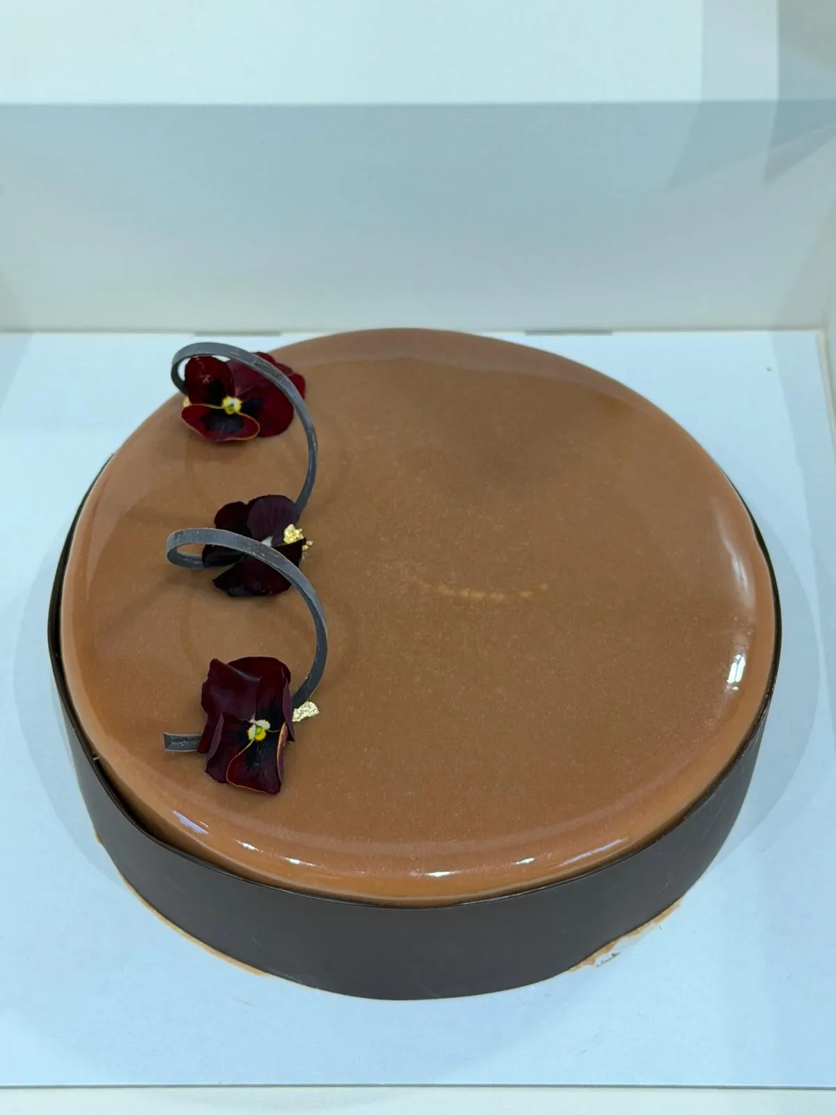 Entremets glaçage miroir caramel, pensées comestibles et copeaux de chocolat
